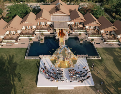 Aerial view of a luxurious Taylor Swift-themed wedding ceremony setup at Balesin Island, with a golden aisle and floral arrangements over a pool.