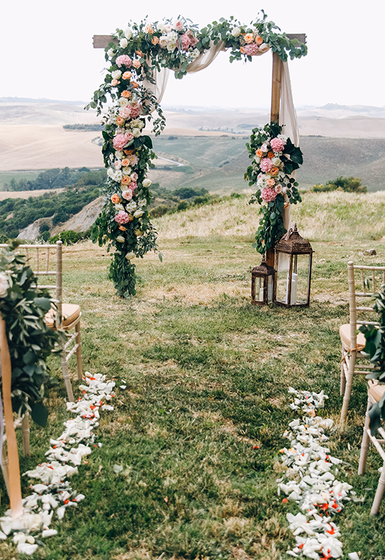 Romantic outdoor wedding ceremony setup with floral arch and scenic countryside view.