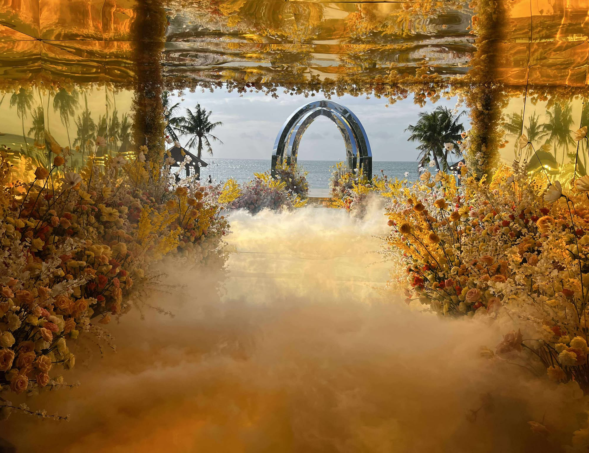 Golden mirrored tunnel lined with pastel florals and mist, leading to a seaside wedding altar at Balesin Island's Taylor Swift-inspired celebration.