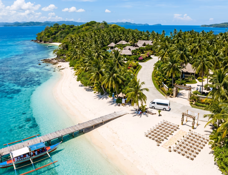 Wide aerial view of a Filipino beach wedding venue on a private island showing white sand ceremony setup wooden dock with a traditional Filipino boat and a van parked near the resort entrance surrounded by palm trees