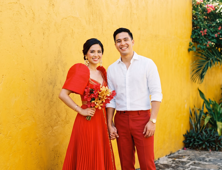 Filipino couple in bold red and white outfits posing against a saturated yellow wall.