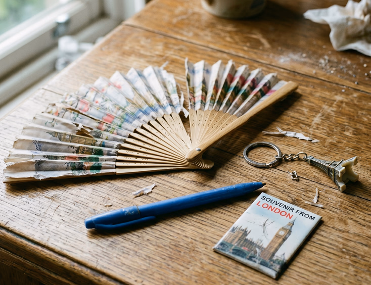 Close-up photo of a cluttered wooden table with discarded and generic debut souvenirs like a torn paper fan and broken keychain.