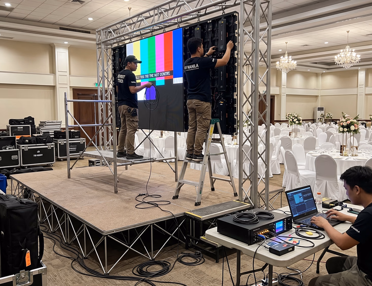 Filipino technical crew assembling modular LED wall panels and testing video processor on stage three hours before wedding reception