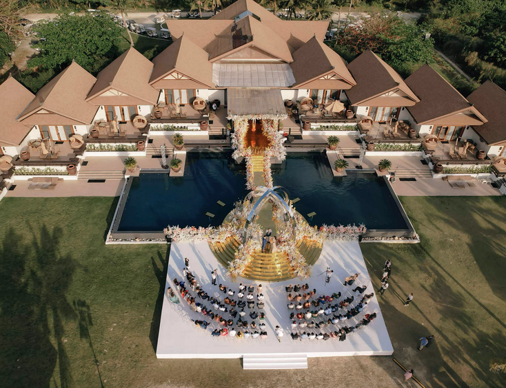 Aerial view of a luxurious Taylor Swift-themed wedding ceremony setup at Balesin Island, with a golden aisle and floral arrangements over a pool.