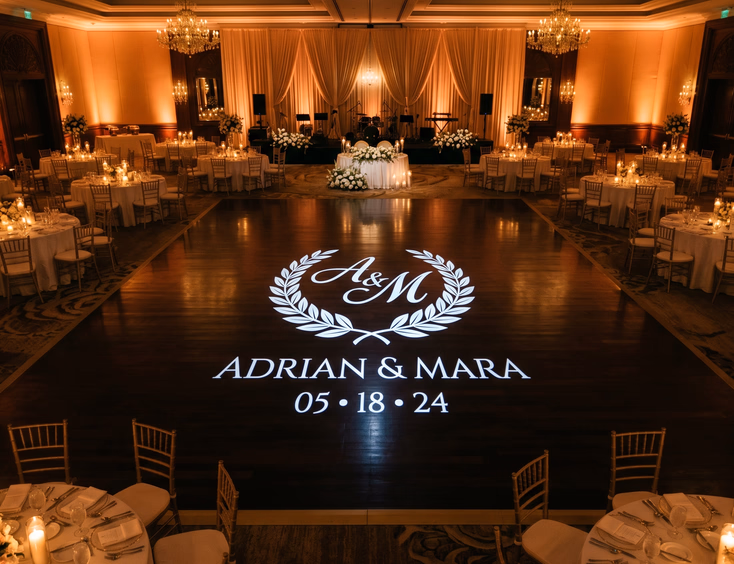 Filipino wedding reception dance floor with crisp white gobo monogram projection, soft amber uplighting, and candlelit guest tables in dimly lit ballroom