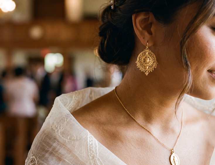 Close-up of Filipino bride's ear and neck wearing gold tamburin earring and Marian medal pendant over sheer piña pañuelo, soft side lighting on gold filigree and woven fabric texture, intimate detail editorial wedding photography