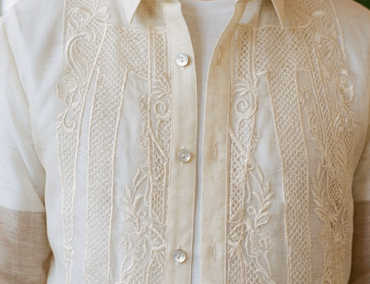 Close-up of intricate calado embroidery and mother-of-pearl buttons on a piña barong tagalog worn by a Filipino groom over a white camisa de chino