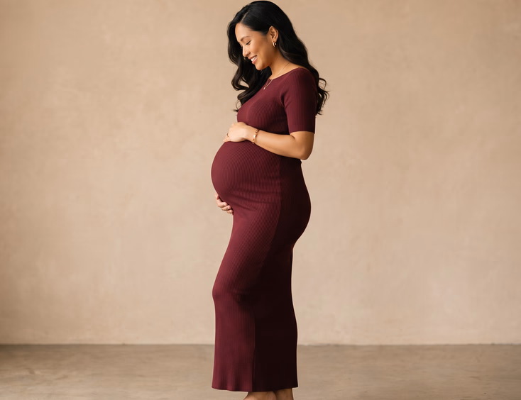 A pregnant Filipino woman poses in a fitted bodycon gown, shown in profile to clearly trace her baby bump against a clean studio backdrop.