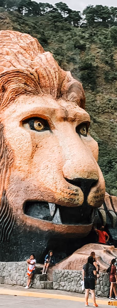 A giant lion head sculpture beside a mountain road with people around