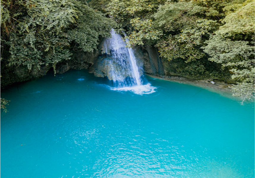 A turquoise blue waterfall surrounded by lush greenery