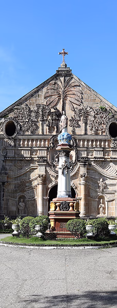 A historic stone church with two towers and detailed facade, surrounded by gardens